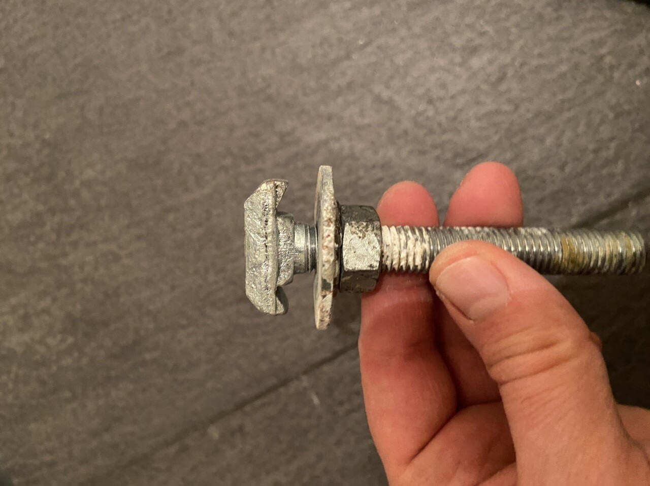 Nahaufnahme einer Hand, die eine Schraube mit Mutter und Unterlegscheibe hält.