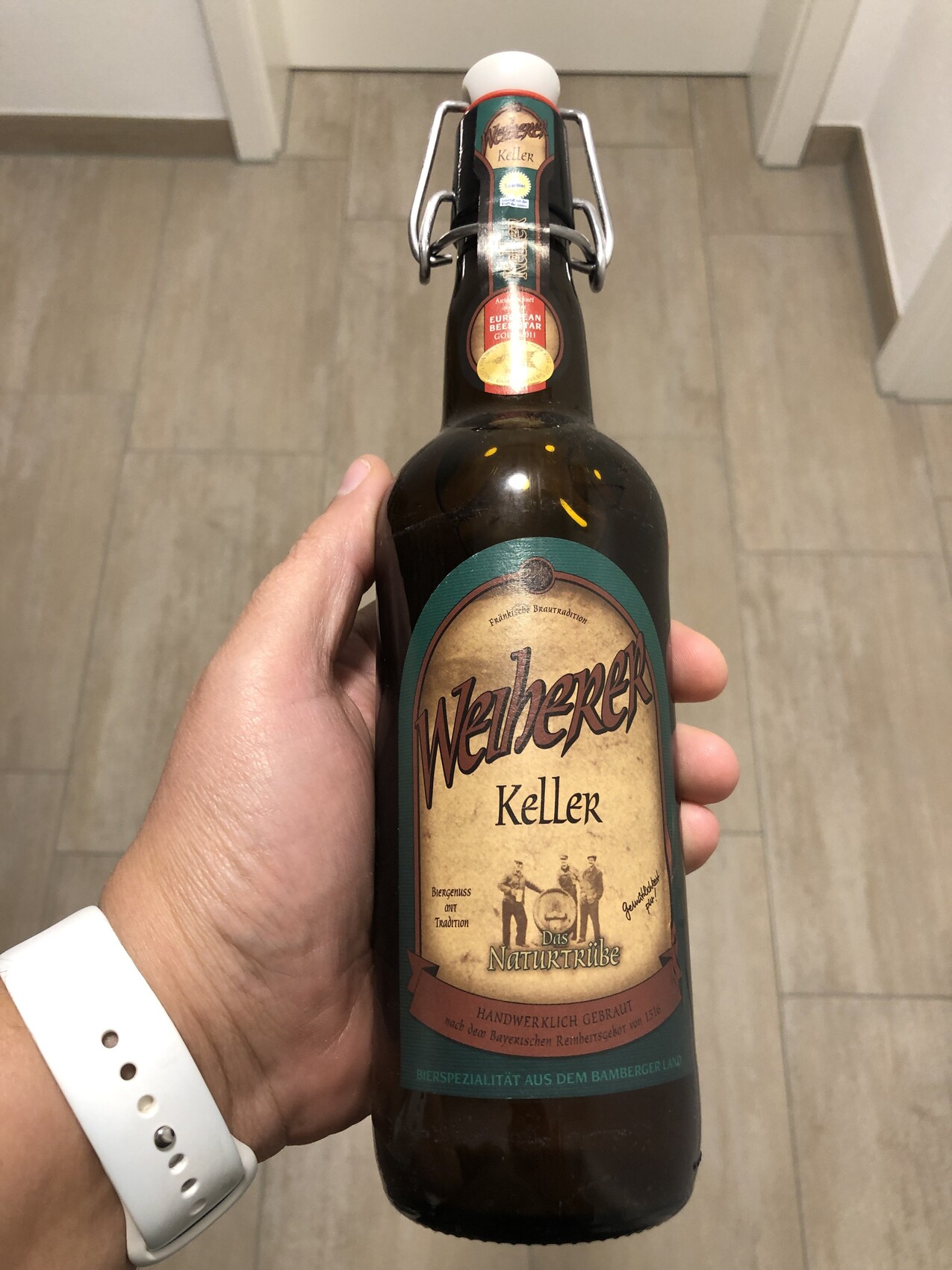 Eine braune Bierflasche mit Swingtop-Verschluss wird von einer Hand gehalten; Etikett liest 'Keller'.