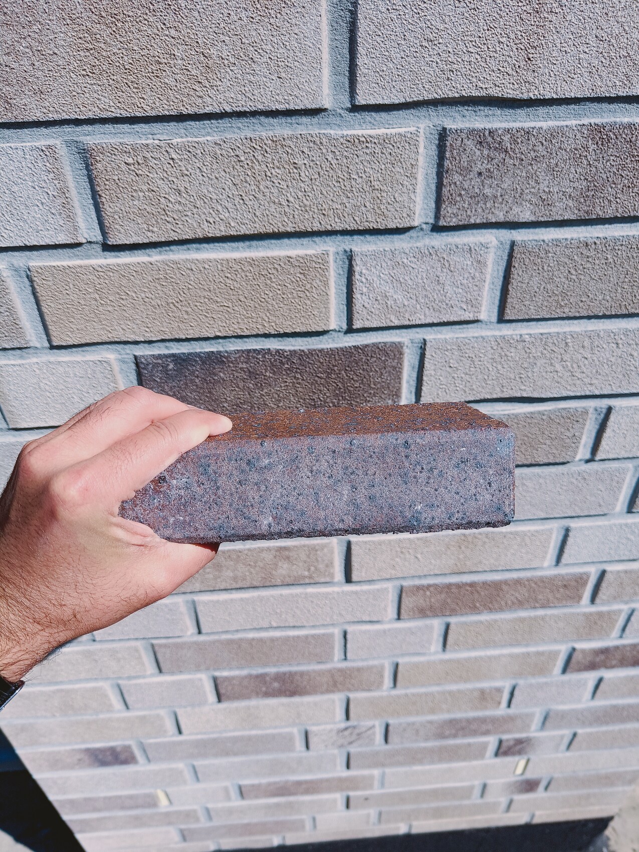 Eine Hand hält einen Backstein vor einer hellgrauen Ziegelwand.