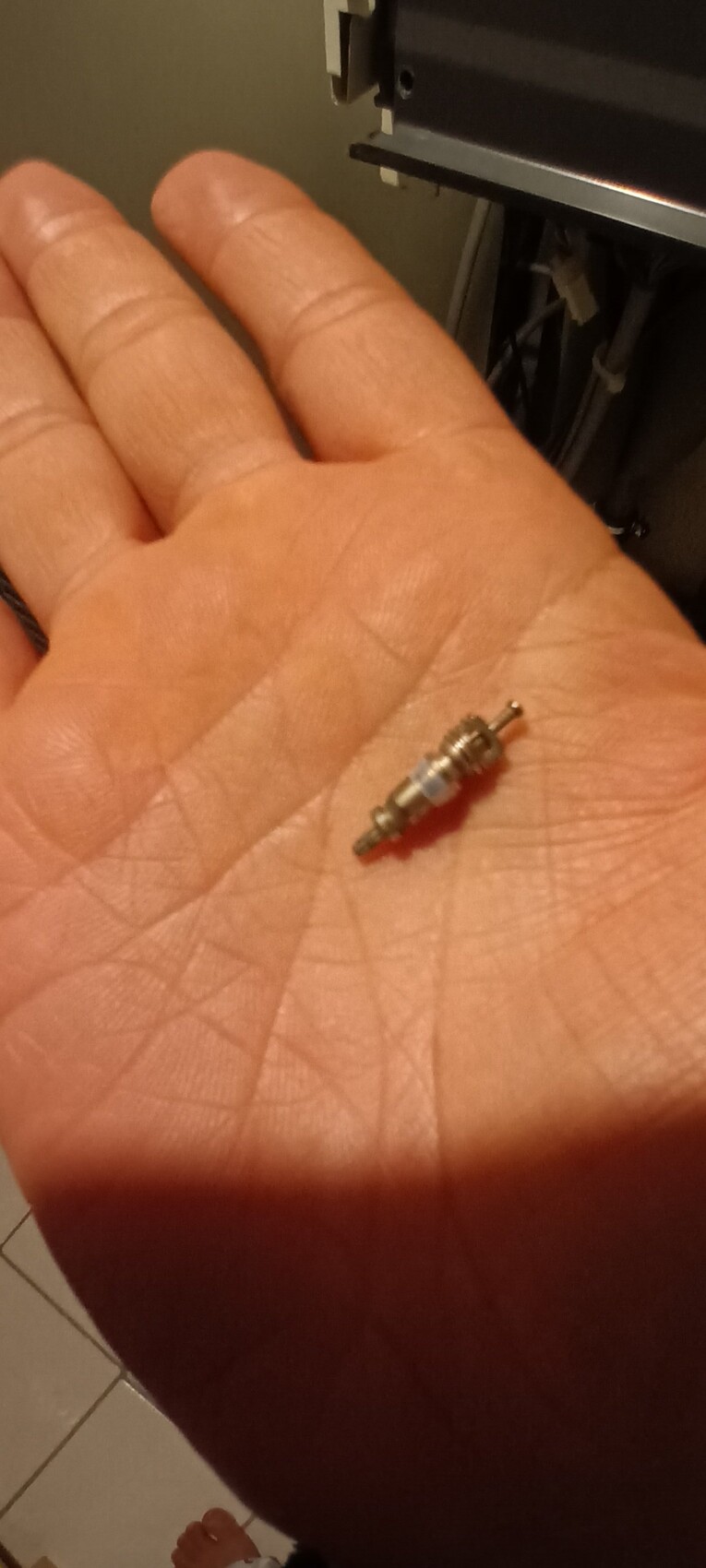 Kleines metallisches Bauteil mit Gewinde und Anschlüssen liegt auf der Handfläche.