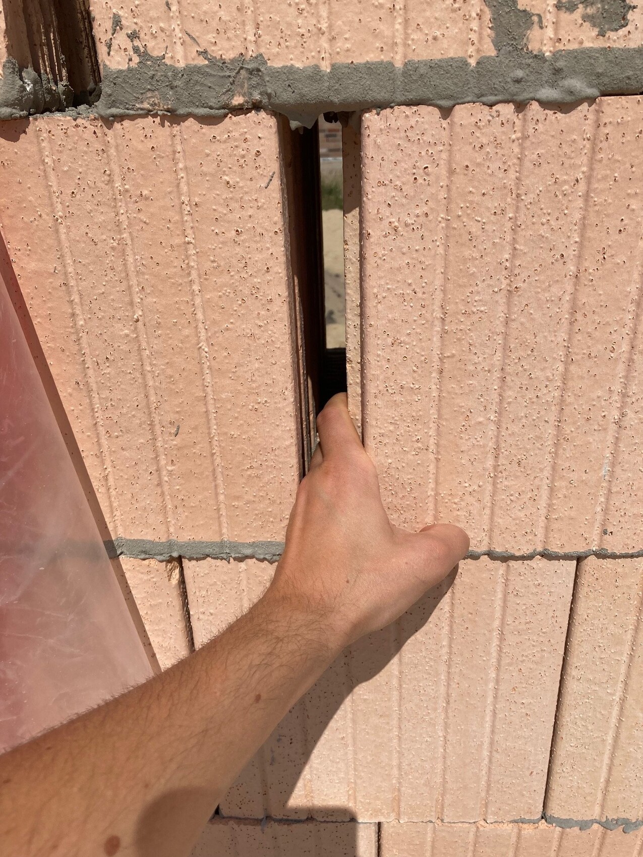 Hand streckt Finger durch schmale Spalte zwischen pinken Betonblöcken, dahinter Blick ins Dunkel