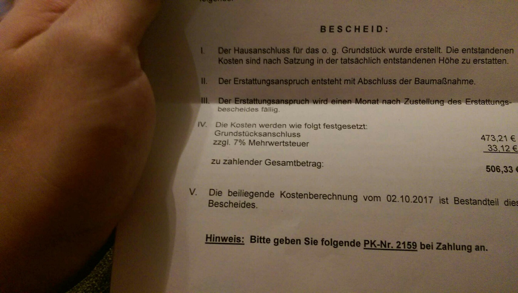 Eine Hand hält einen gedruckten Bescheid mit Kostenangaben und Textzeilen.