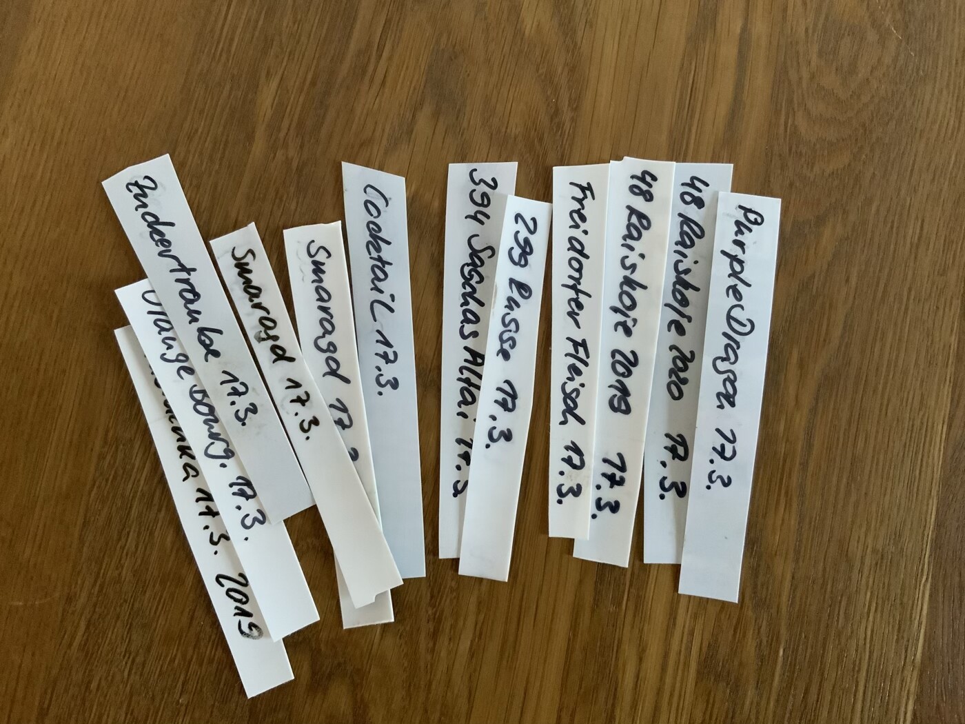 Mehrere weiße Papierstreifen mit handschriftlichen Wörtern liegen auf einem Holztisch.