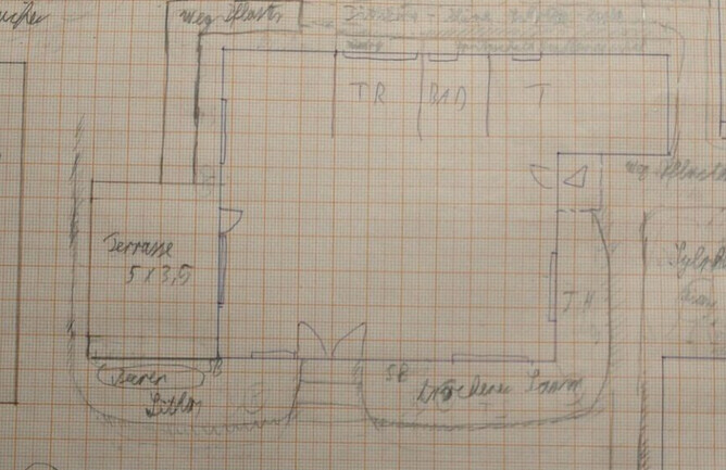 Handgezeichnete Grundriss-Skizze eines Hauses mit Terrasse, Wohnzimmer und Flur auf kariertem Papier.