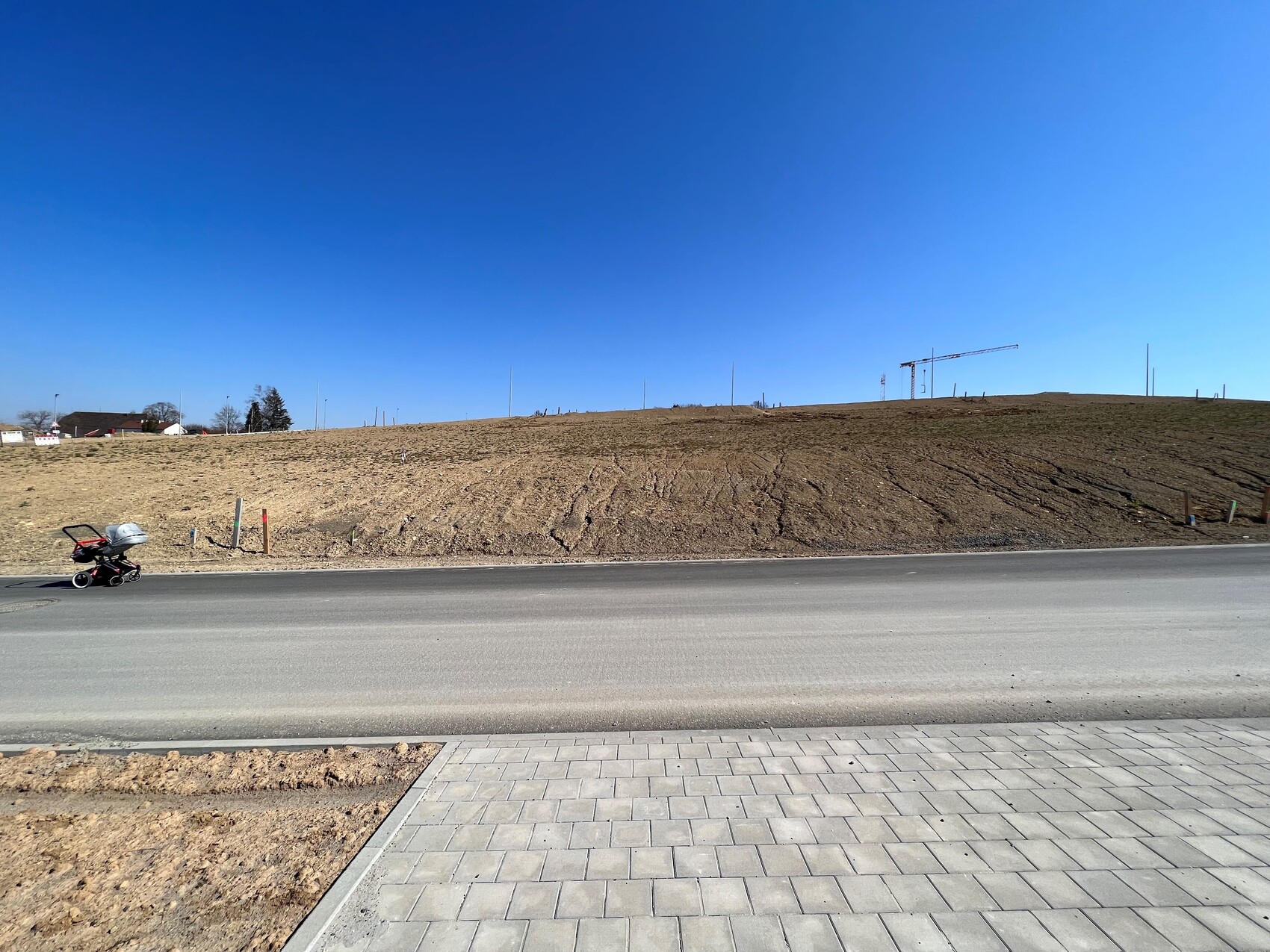 Karger Erdhügel neben einer Straße, Baukran am Horizont, Kinderwagen links im Vordergrund