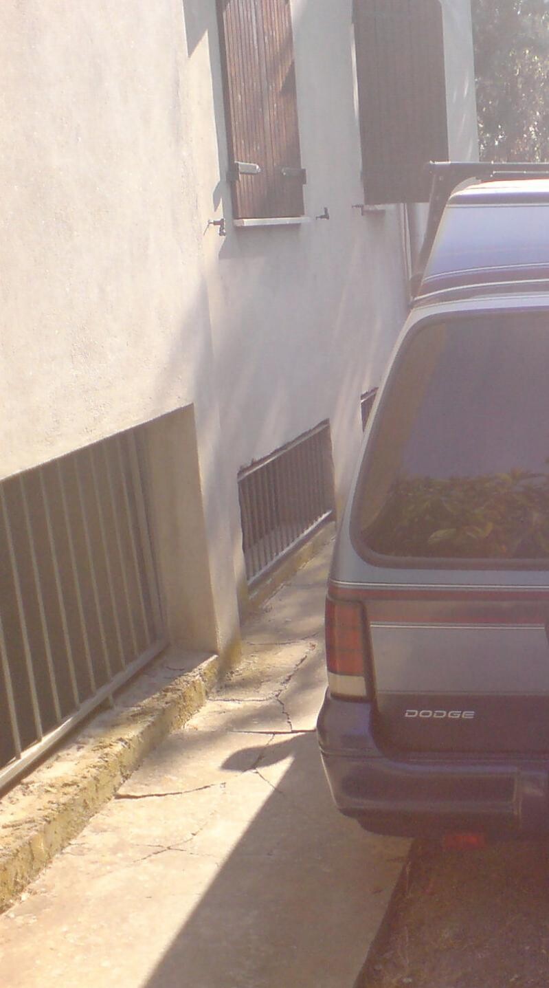 Außenansicht eines Hauses mit Fensterläden und parkendem Auto an schmaler Straße.