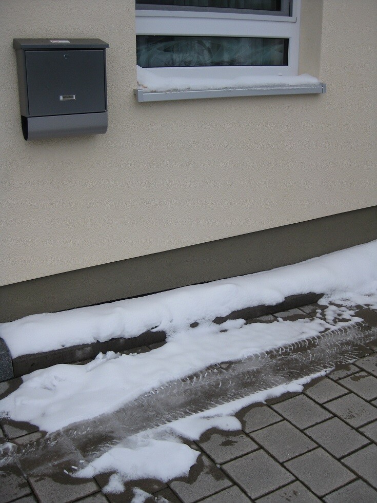 Außenwand eines Hauses mit Fenster, Briefkasten und Schnee am Boden.