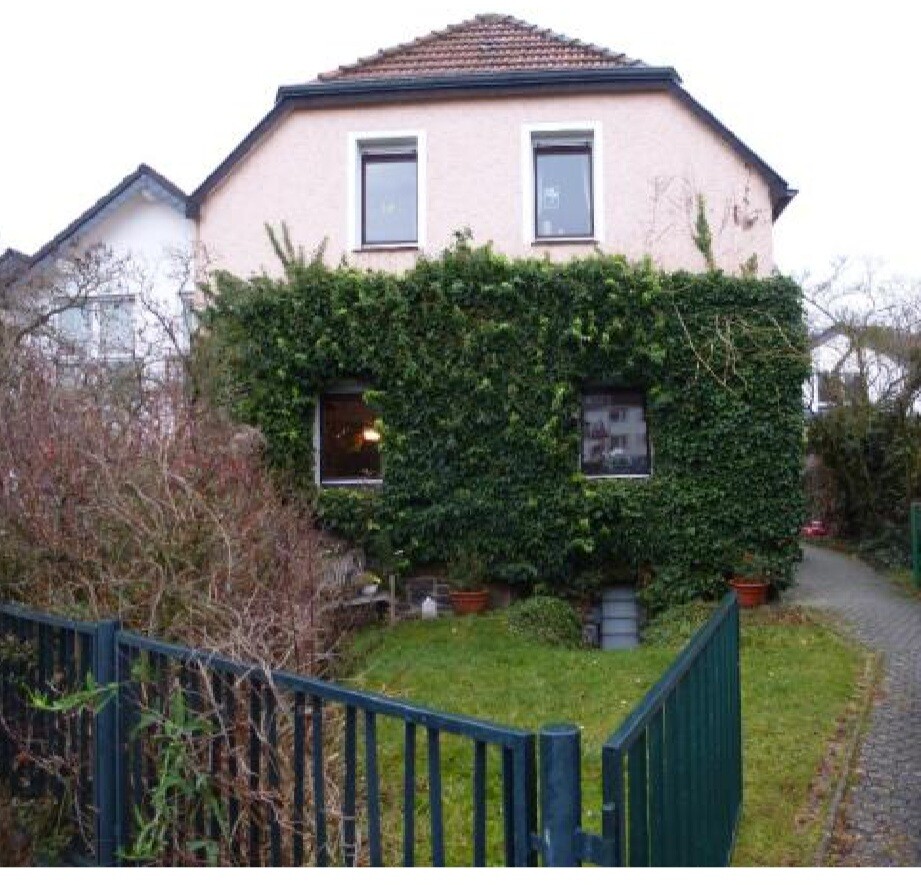 Zweistöckiges Haus mit vollständig von Efeu bedeckter Fassade, Garten und Zaun.