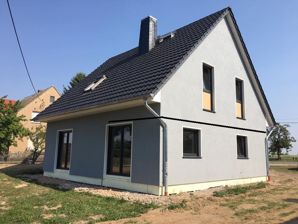 Zweistöckiges Haus mit Satteldach, grauer Fassade und mehreren Fenstern.