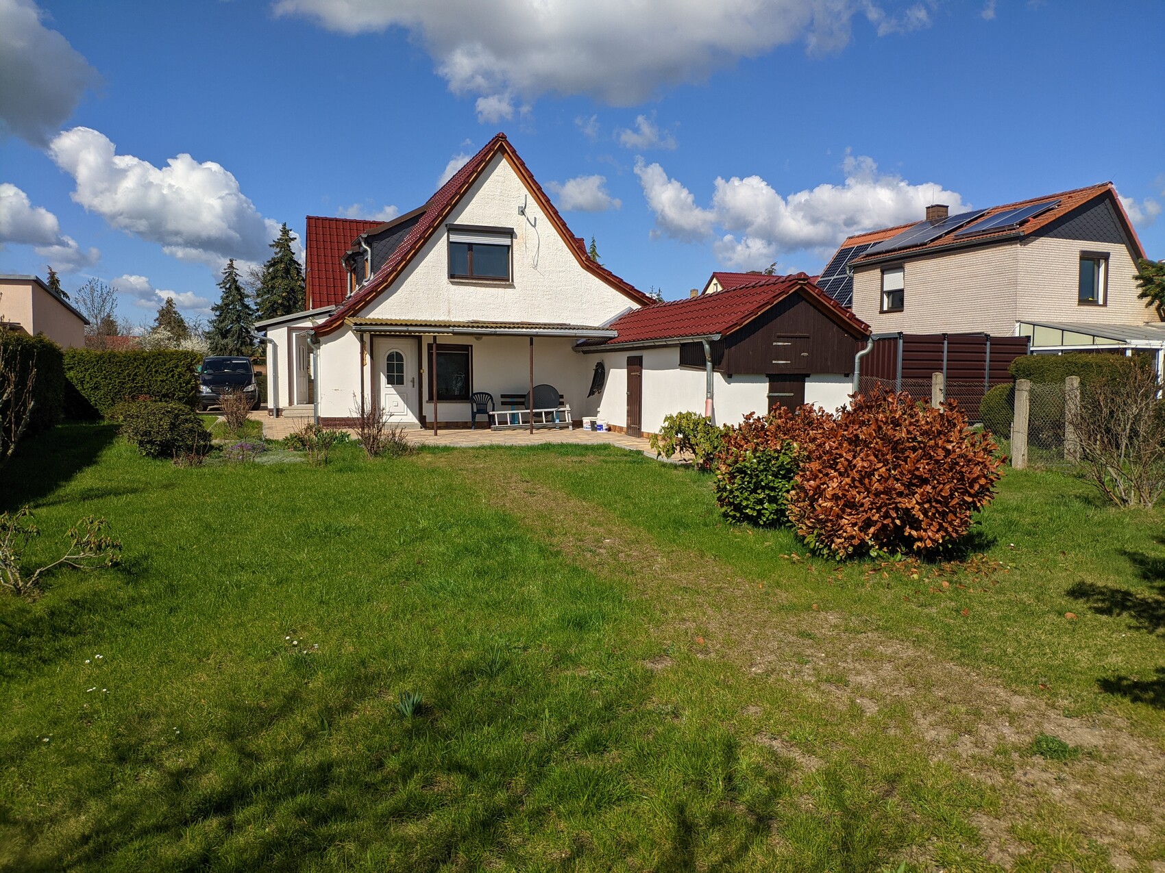 Außenansicht eines Einfamilienhauses mit rotem Dach, Terrasse und Garten.