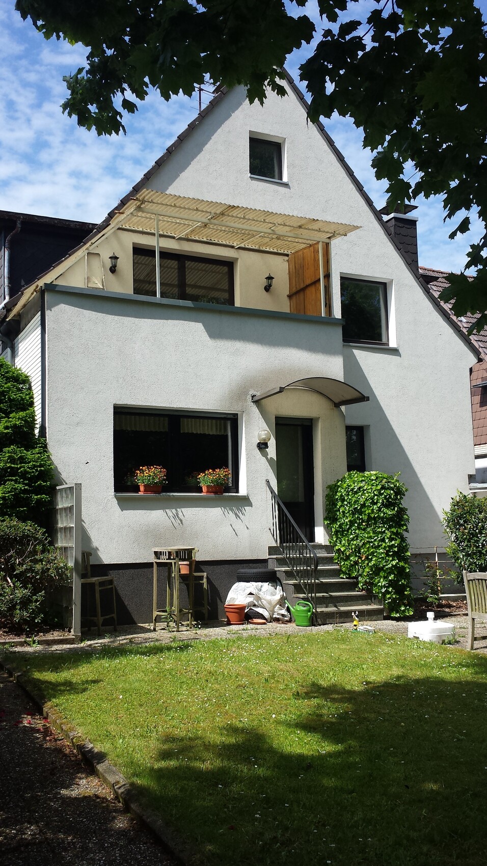 Weiße zweigeschossige Hausfassade mit Terrasse, Eingangstreppe und Garten.