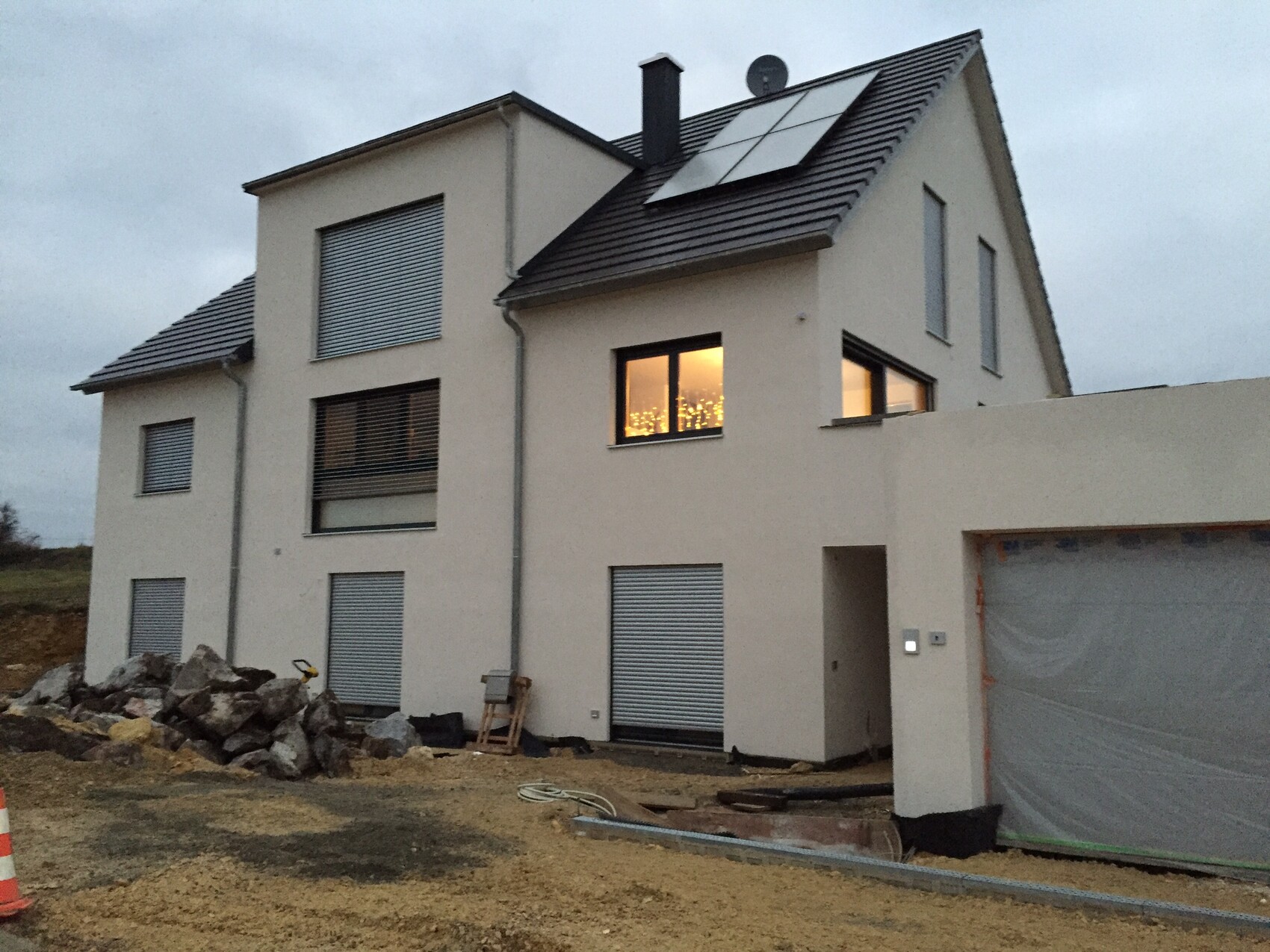 Weisses Einfamilienhaus unter Bau mit Solarmodule auf dem Dach; Steine und Baugeräte vorne