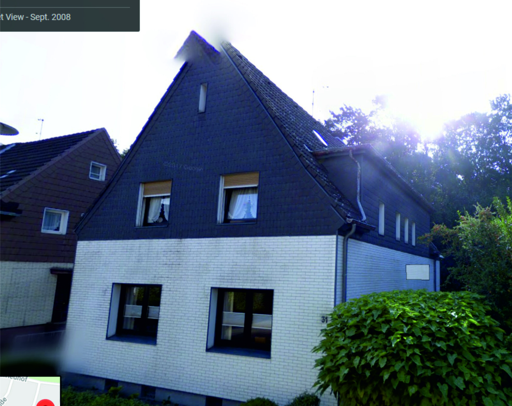 Außenansicht eines Wohnhauses mit dunklem Spitzdach, weißer Fassade und Garten.
