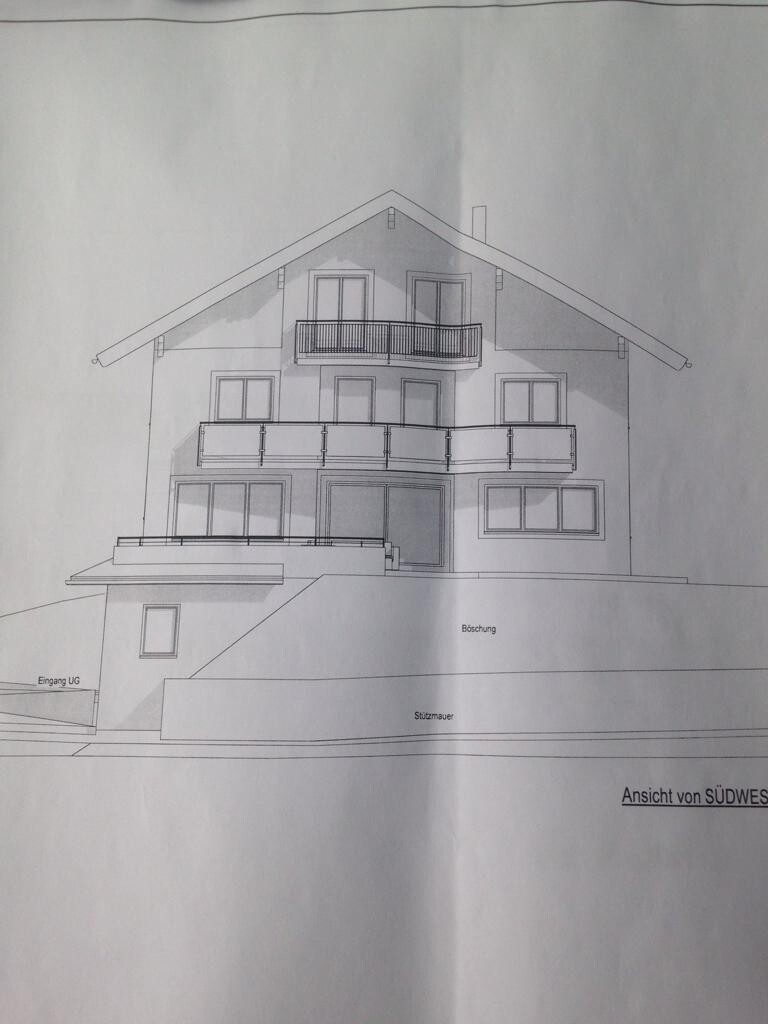 Ansicht eines mehrstöckigen Hauses mit Balkonen, Hanglage und Terrasse.