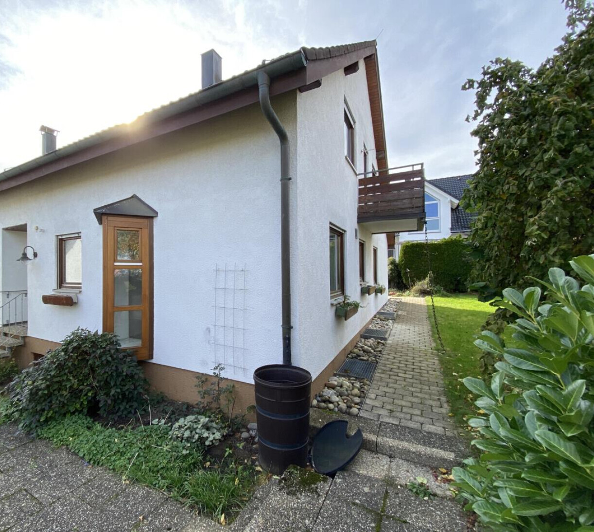 Außenansicht eines weißen Hauses mit Balkon, Gartenweg und Pflanzen