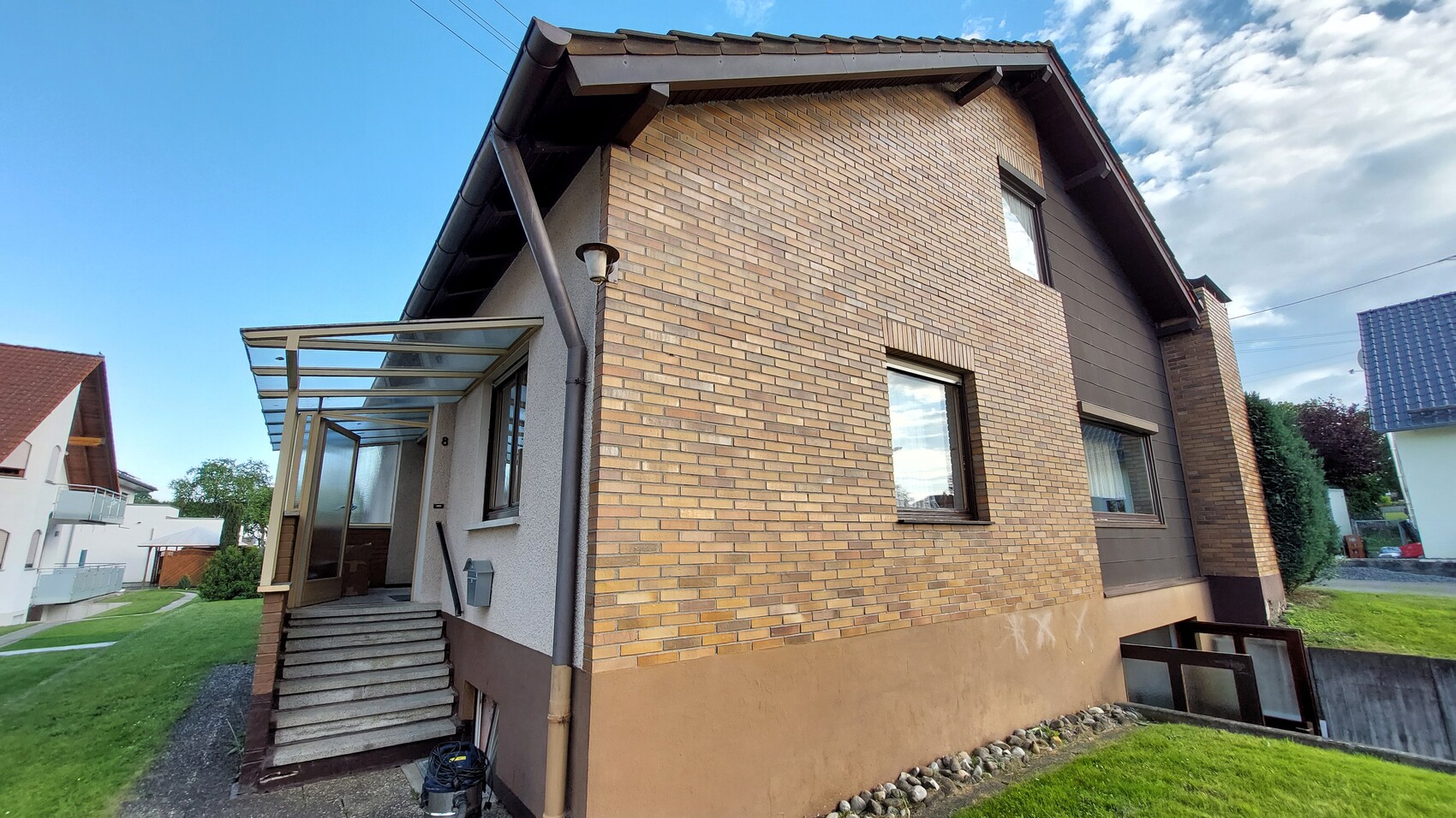 Außenansicht eines zweistöckigen Hauses mit gelb-braunen Klinkerwänden, Treppe und Glasvordach