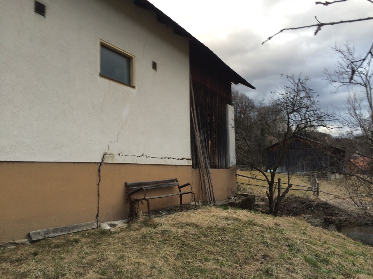 Außenwand mit Riss, Holzwandbereich und verlassene Gartenbank im ländlichen Hof