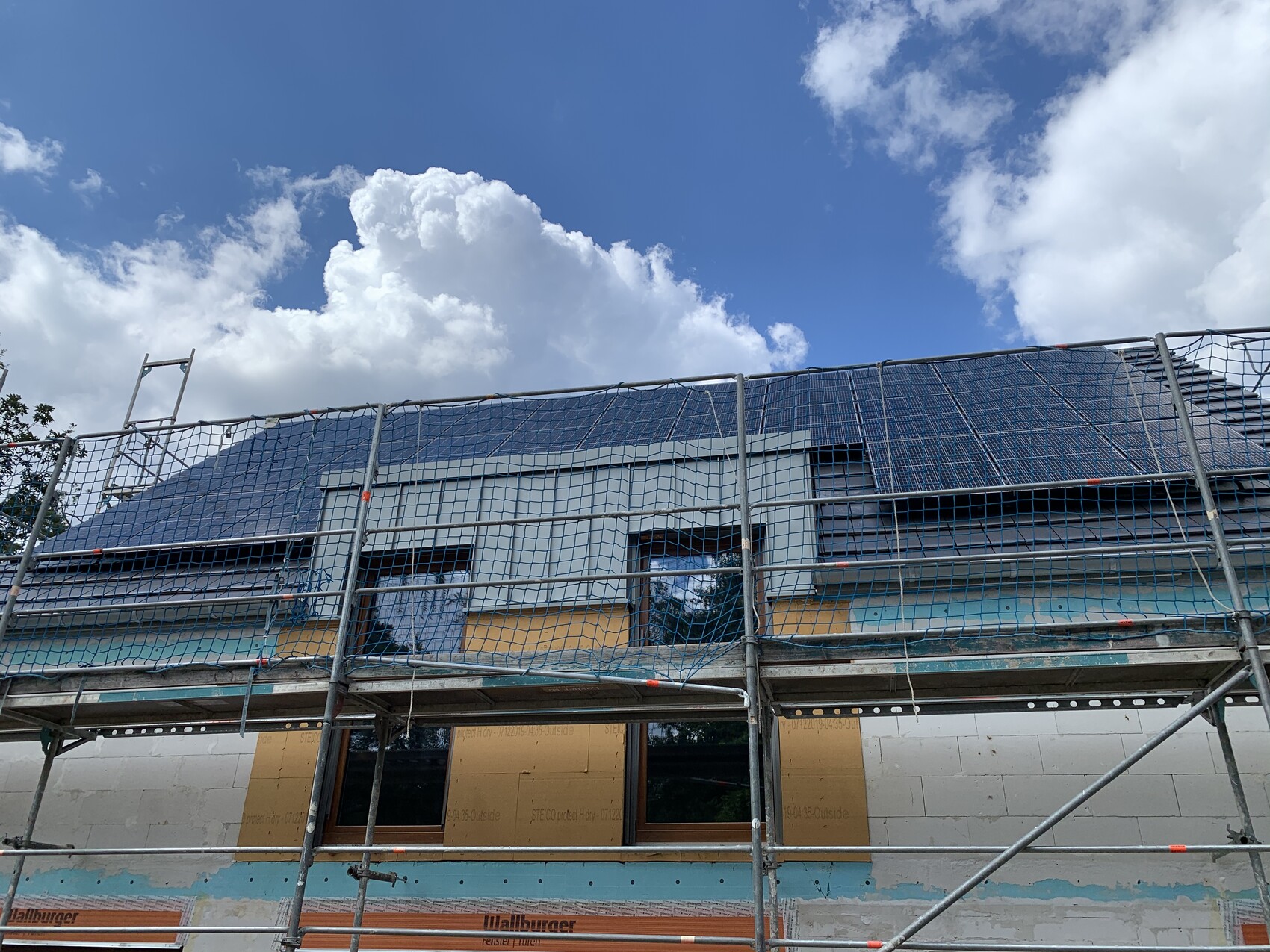 Baustelle am Haus mit Gerüst, Fenster, Dach mit Solarpaneele, blauem Himmel und Wolken