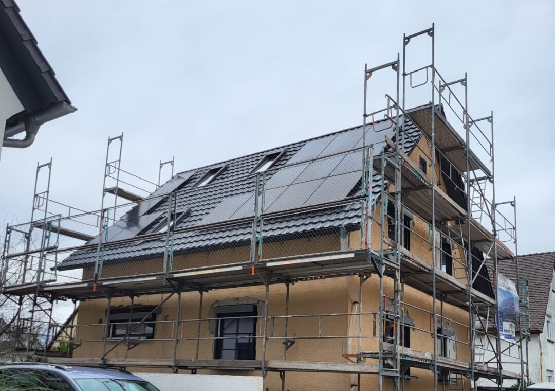 Zweistöckiges Haus mit Baugerüst; Dach mit Solarmodulen in Bauphase.