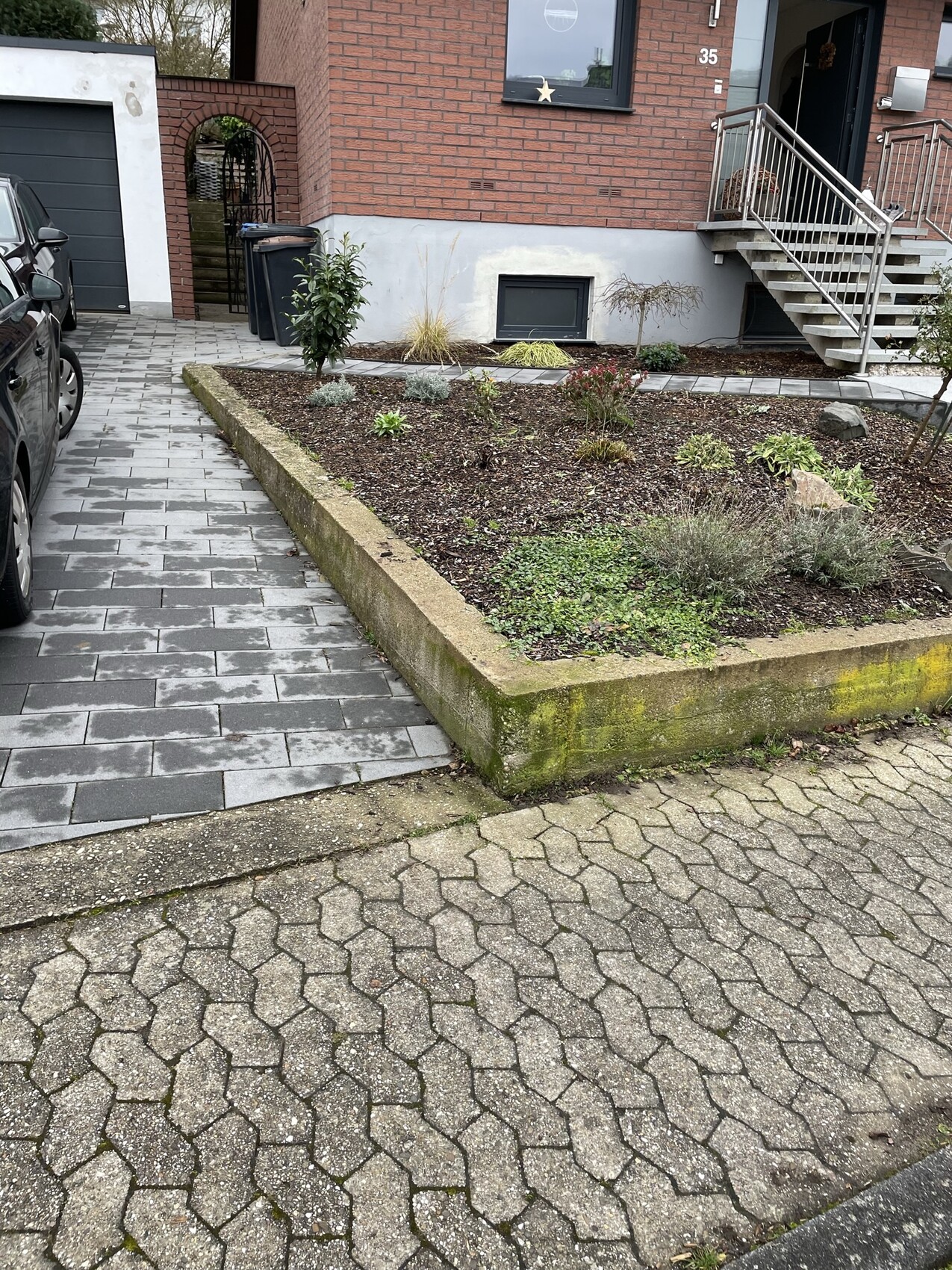 Vorderansicht eines roten Backsteinhauses: Pflasterweg, Beet, Treppe zur Tür, geparkter Wagen links.