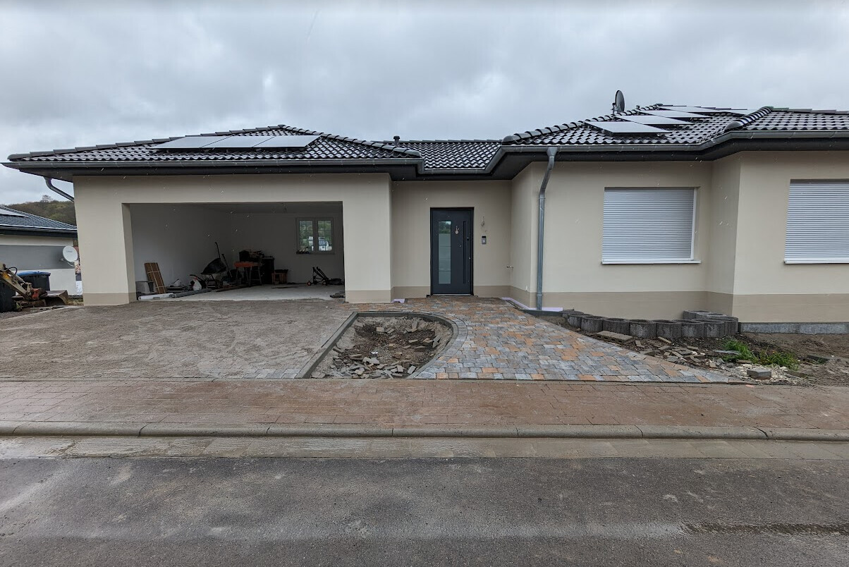 Frontansicht eines Neubau-Hauses mit Garage, Eingangstür und gepflastertem Vorplatz