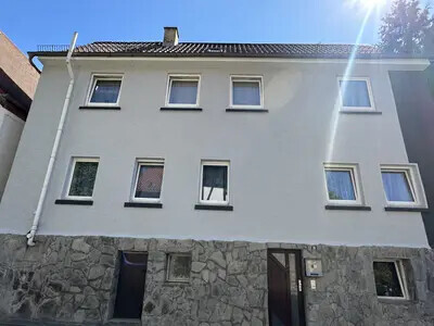 Zweigeschossiges Wohnhaus mit weißer Fassade und steinernem Untergeschoss – Frontansicht.