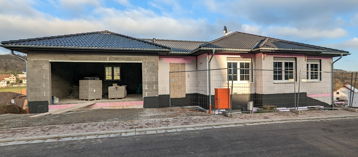 Neubau eines Einfamilienhauses mit offener Garage, Baustelle, Bauzäune und Baumaterialien.