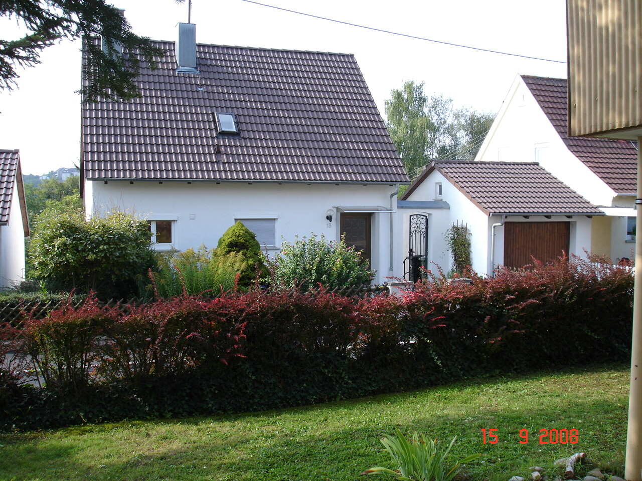 Vorderansicht eines weißen Einfamilienhauses mit dunklem Ziegeldach und Garten.