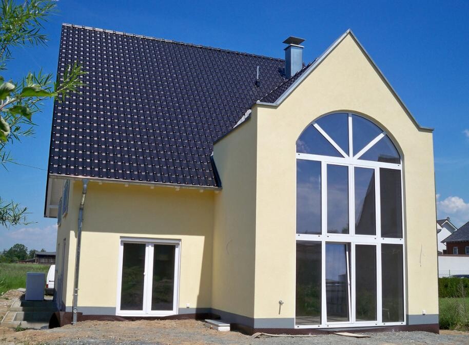 Vorderansicht eines gelben Hauses mit großem Bogenfenster und dunklem Dach.