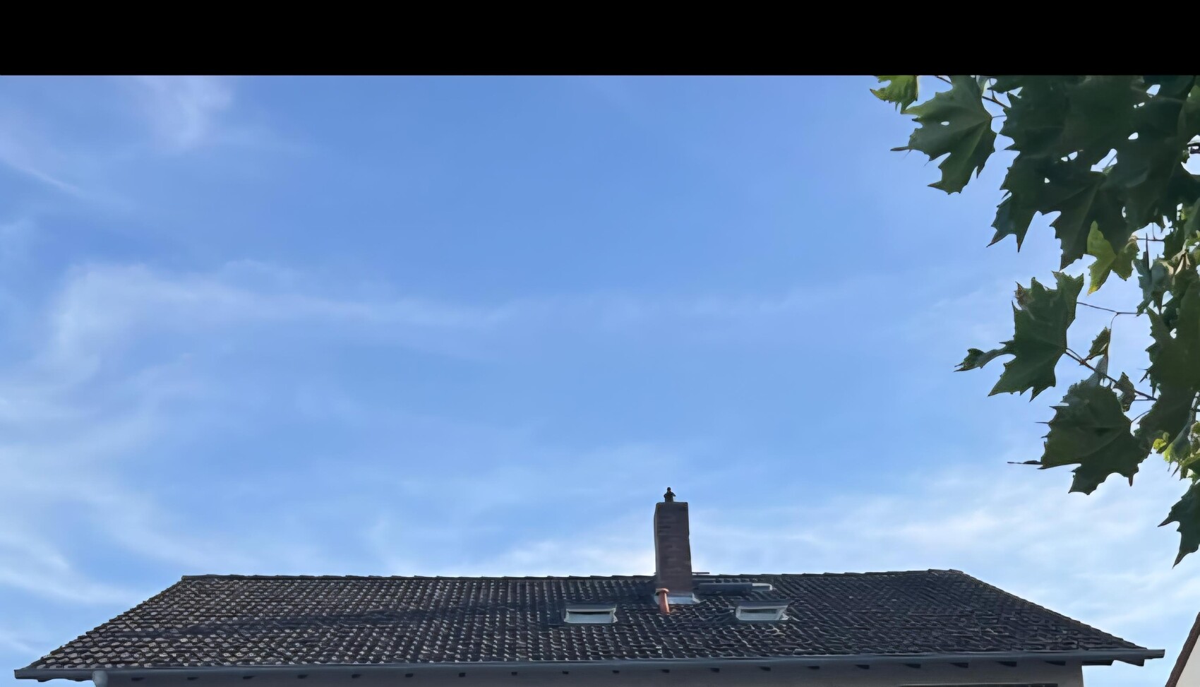 Außenansicht eines Hauses mit Ziegel-Dach, Kamin und blauem Himmel.