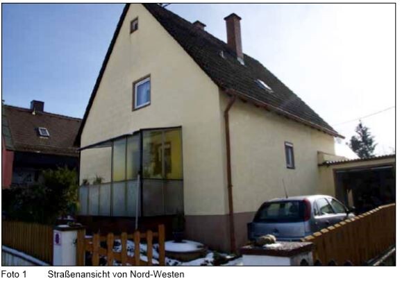 Zweistöckiges gelb-beiges Haus mit Glasveranda, davor Auto und Holzzaun; Nordwestansicht