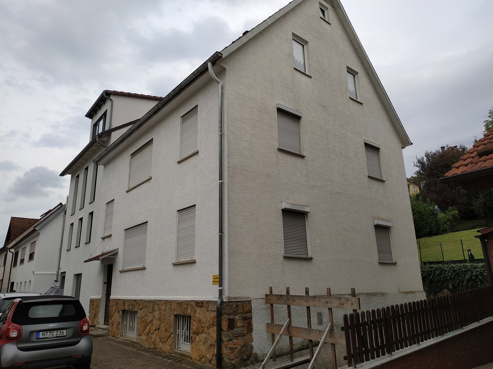 Mehrfamilienhaus mit weißer Putzfassade, geschlossene Rollläden, Dachspitze