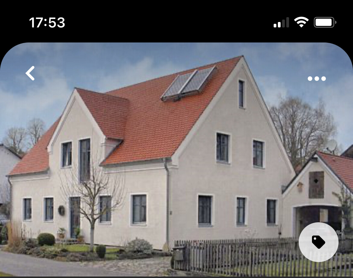 Helles Einfamilienhaus mit rotem Satteldach, Solarpaneele, kleinem Garten und Holzzaun.
