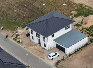 Vogelperspektive: Weißes Haus mit grauem Dach und Garage auf Baugrundstück