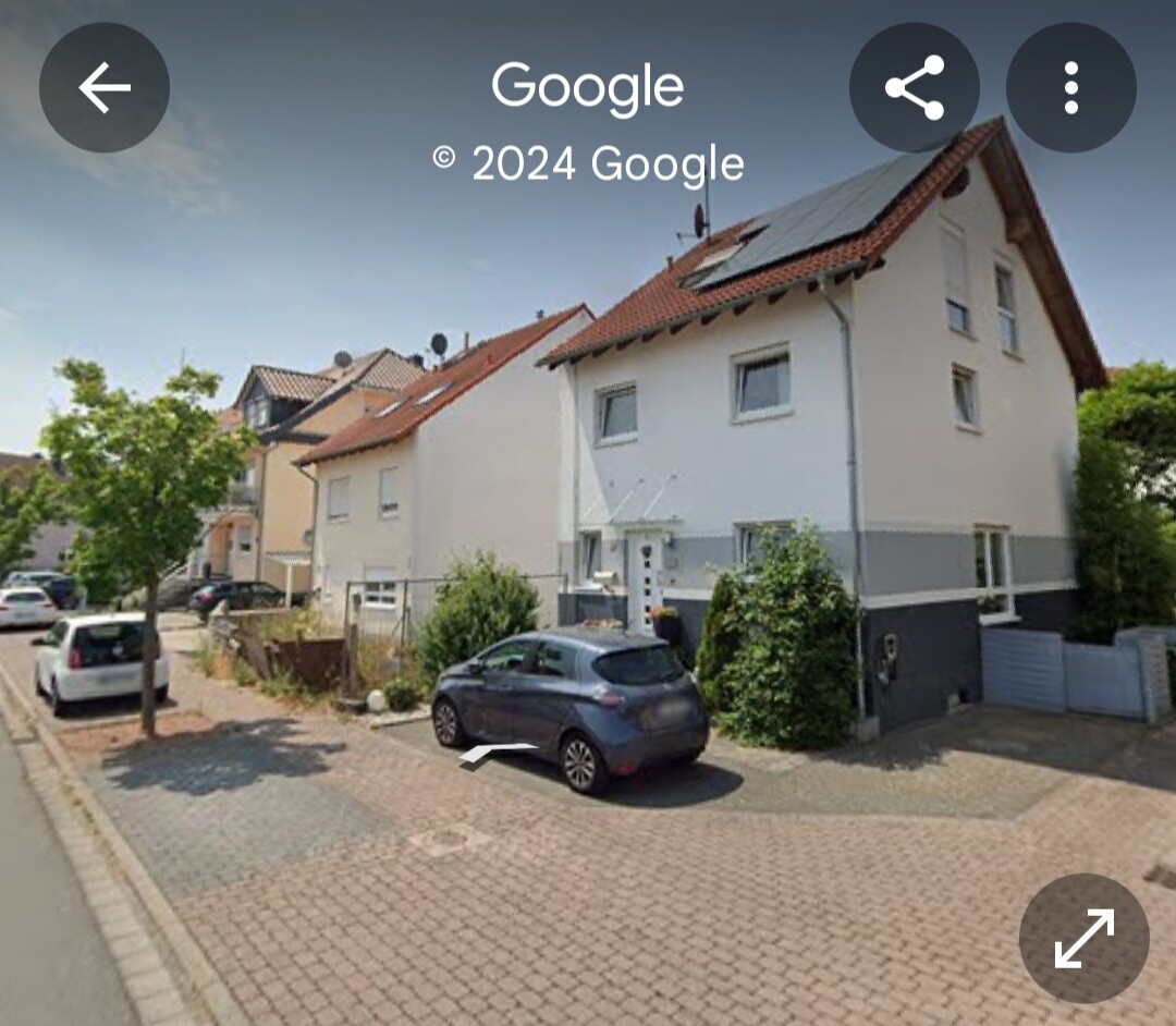 Straße mit hellen Reihenhäusern, geparktem Auto vorne und Bäumen am Straßenrand