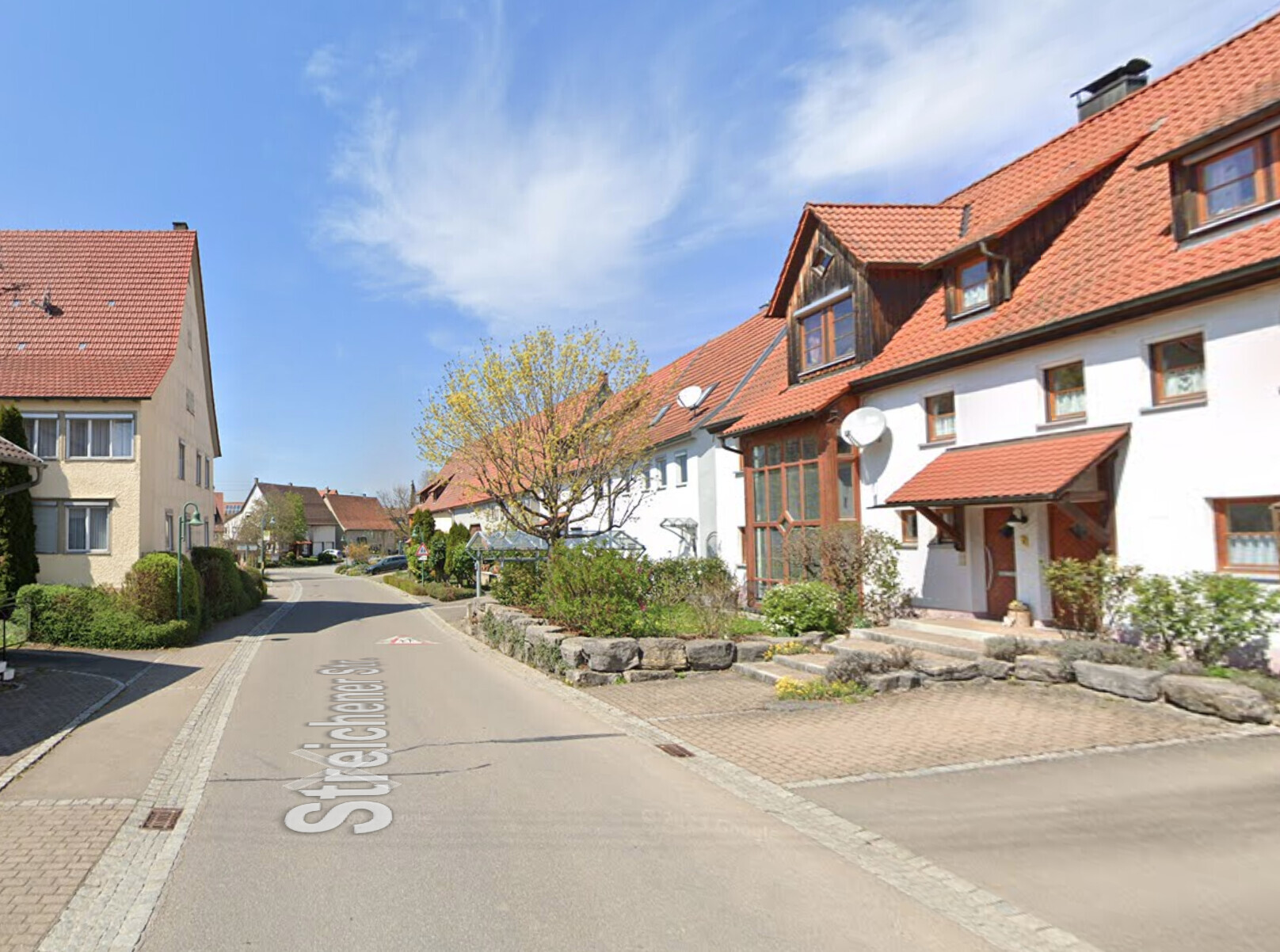 Wohnviertel mit Häusern, roten Ziegeldächern, Bäumen und Gehwegen.