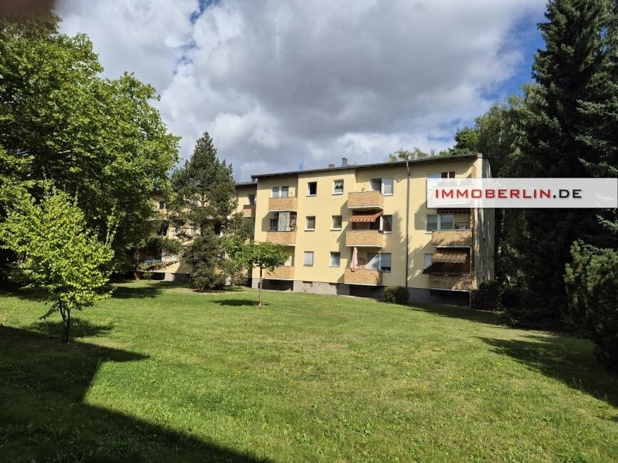 Mehrfamilienhaus mit gelber Fassade, grünem Garten und Bäumen, Logo IMMOBERLIN.DE