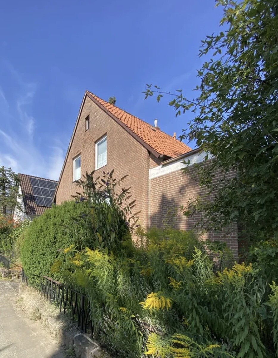 Außenansicht eines roten Ziegelhauses mit grünem Garten und blauem Himmel
