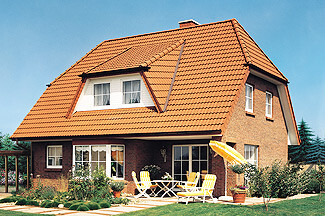 Zweistöckiges rotes Ziegelhaus mit Satteldach, große Terrasse und Gartenmöbel.