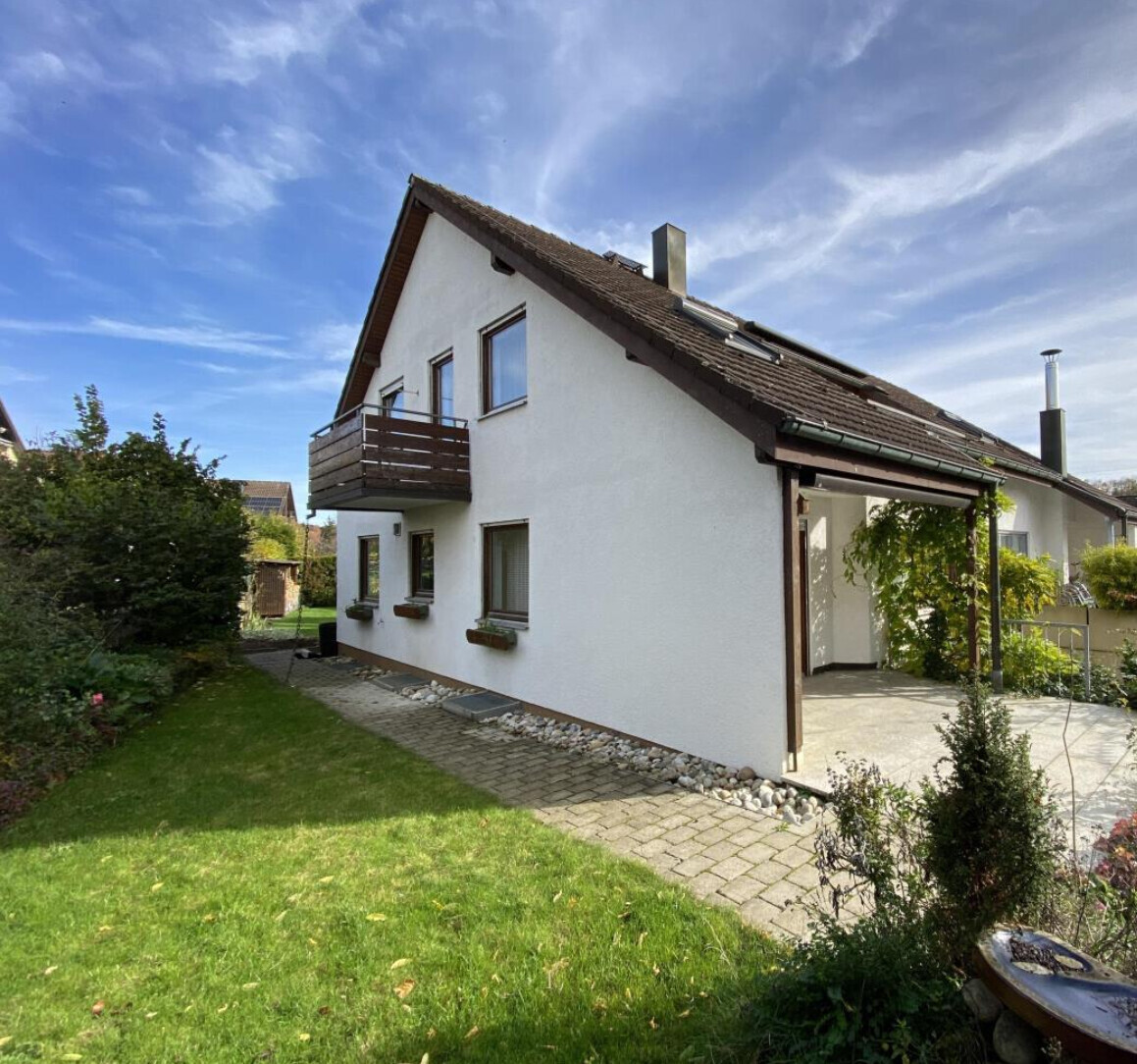 Zweistöckiges weißes Einfamilienhaus mit Balkon, Garten und Zufahrt.