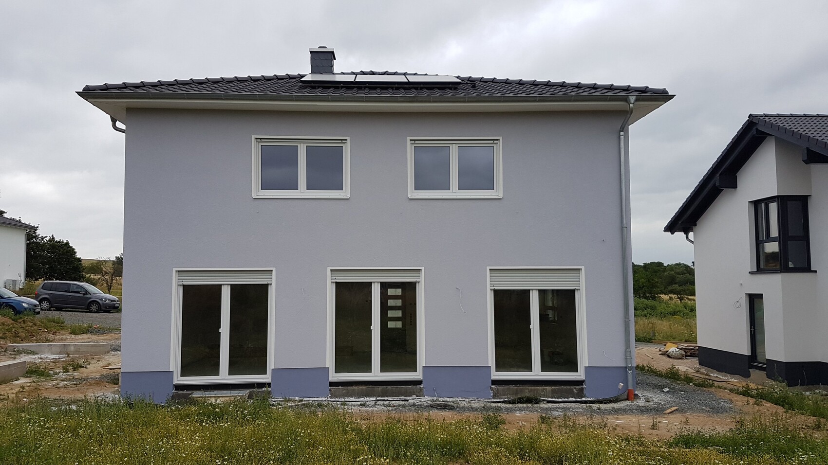 Zweistöckiges graues Wohnhaus mit drei großen Glas-Schiebetüren und Solaranlage auf dem Dach.