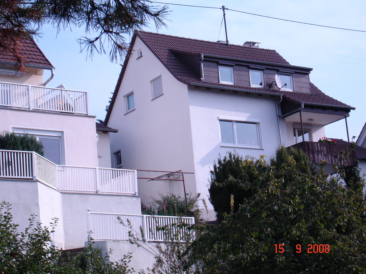 Mehrstöckiges weißes Wohnhaus mit Balkon, Gartenbereich und umliegendem Grün.