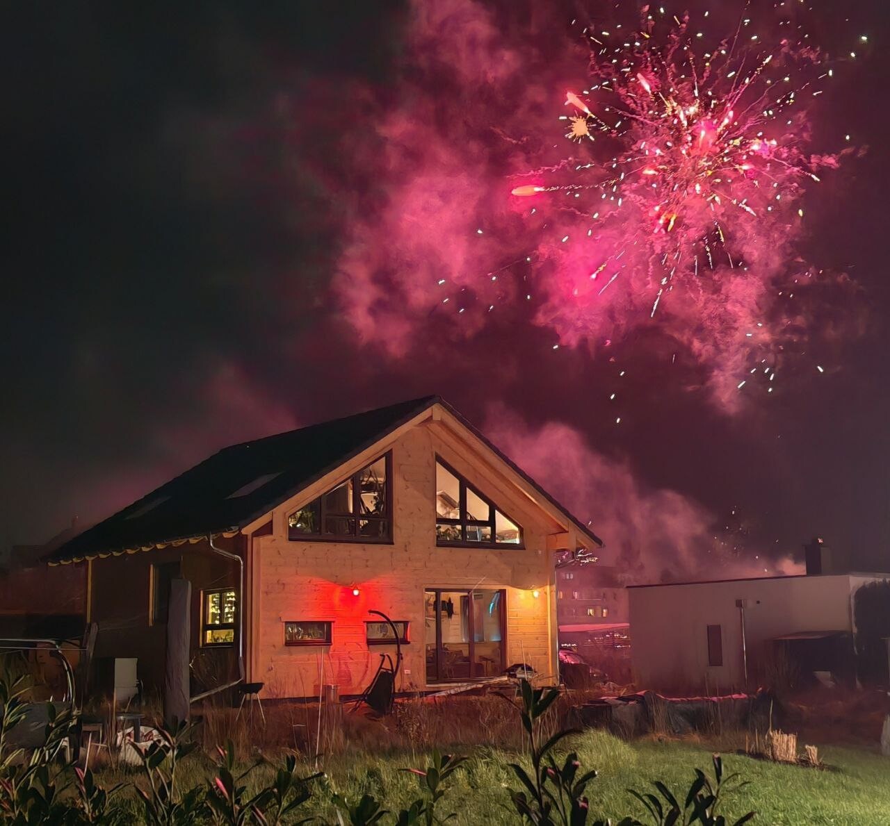 Modernes Haus bei Nacht mit pinkem Feuerwerk am Himmel über dem Garten.