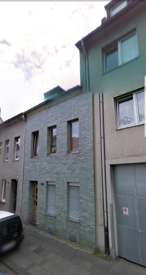 Außenansicht eines Reihenhauses mit grauer Backsteinfassade und Fenstern.
