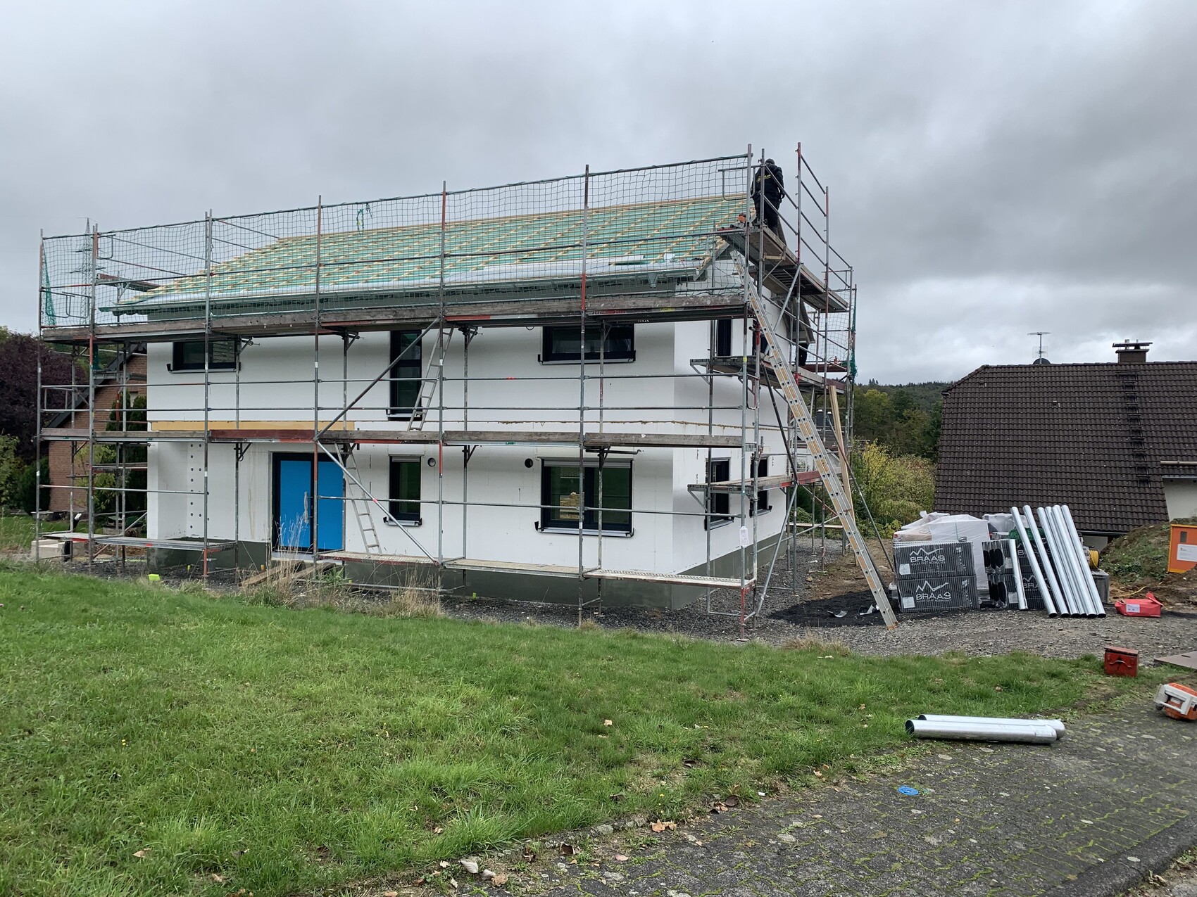 Zweistöckiges Haus im Bau mit Gerüst, Dacharbeiten und Arbeiter oben.