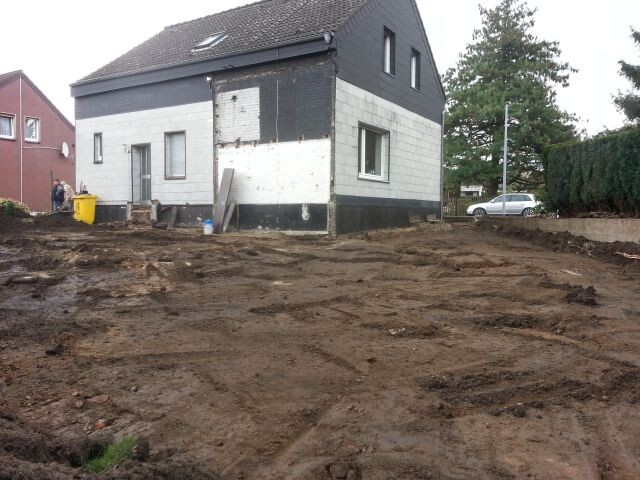 Baugrube und Erdarbeiten vor einem halbfertigen Haus auf einer Baustelle