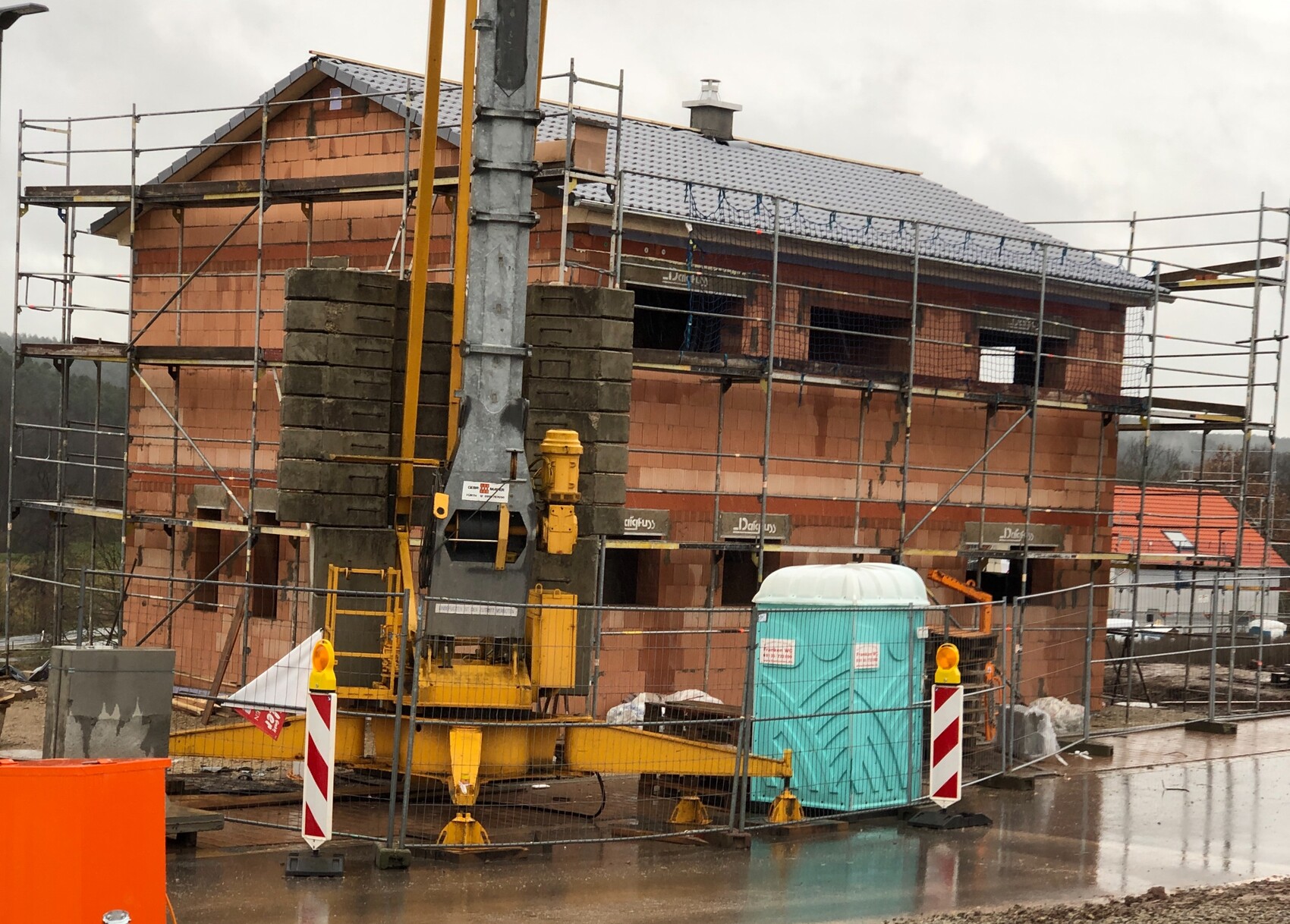 Baustelle mit Rohbau, Geruesten, gelbem Baugeraet und portabler Toilette