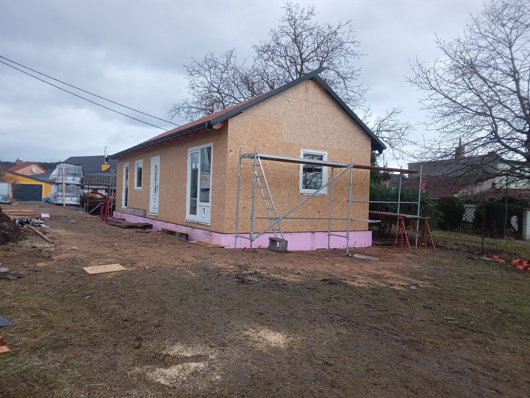 Kleines Haus im Rohbau mit OSB-Verkleidung, pinker Fundamentdämmung und Baugerüst.
