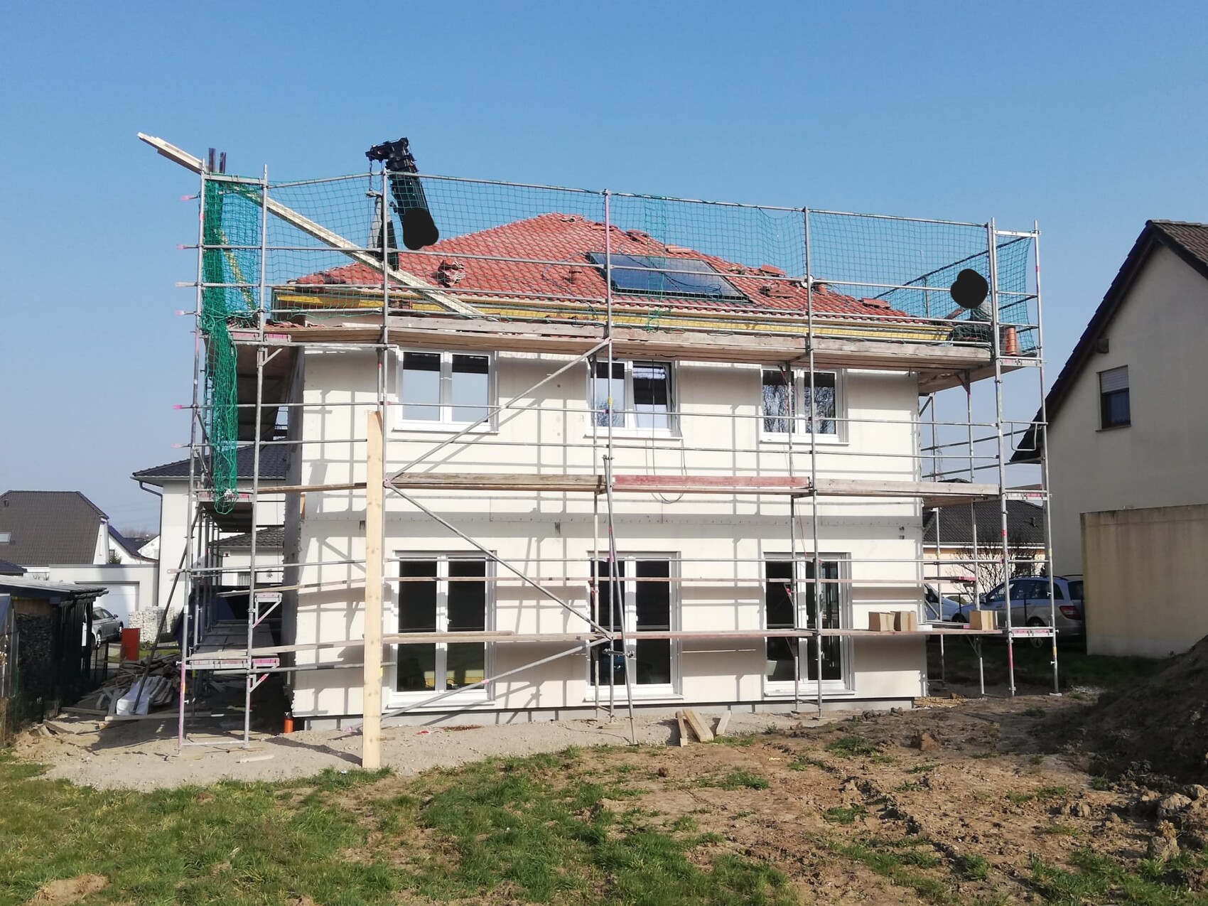 Zweistöckiges Haus mit Gerüst um das Dach, Bauarbeiten am Dach und an der Fassade, blauer Himmel.