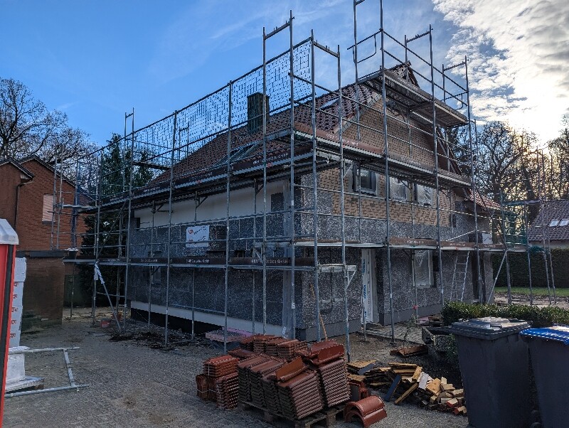 Zweigeschossiges Haus im Rohbau mit Gerüst rundum und Baumaterialien davor